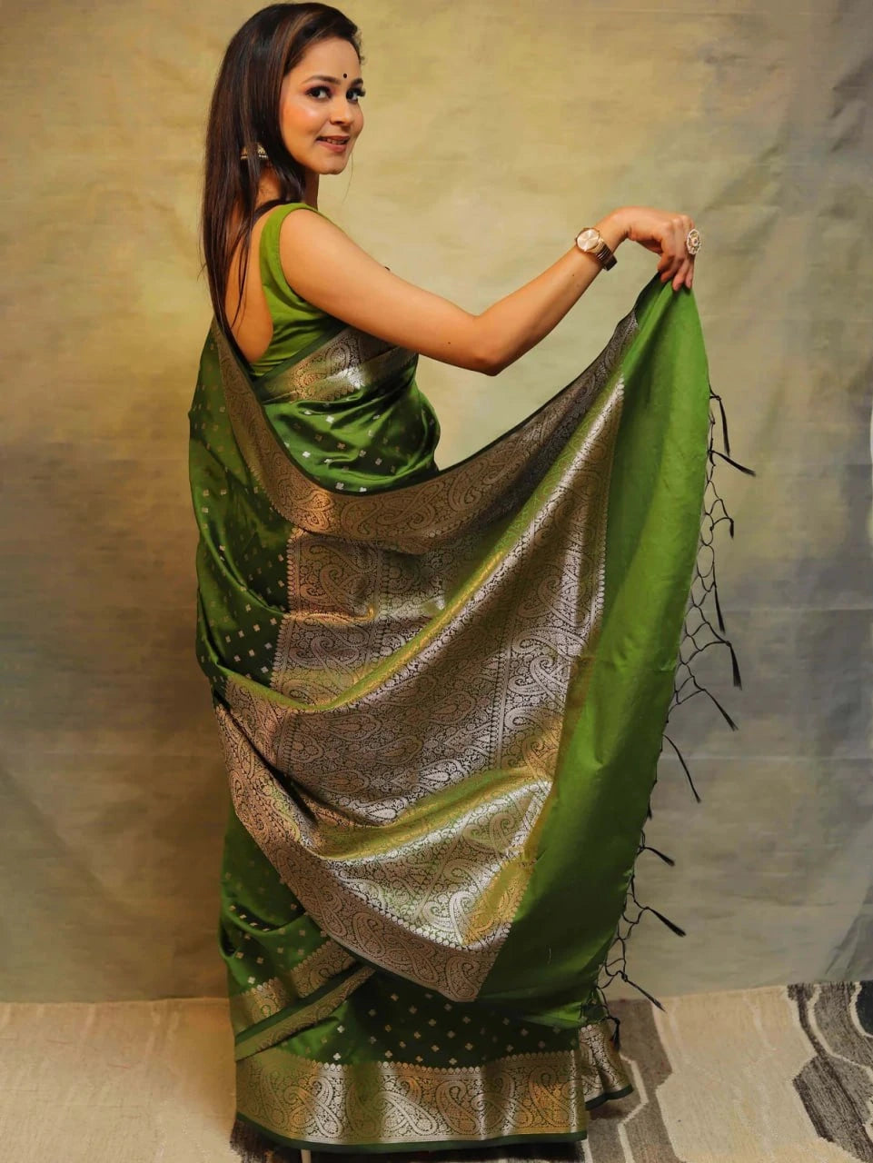 Woman holding a green and silver saree against a neutral background