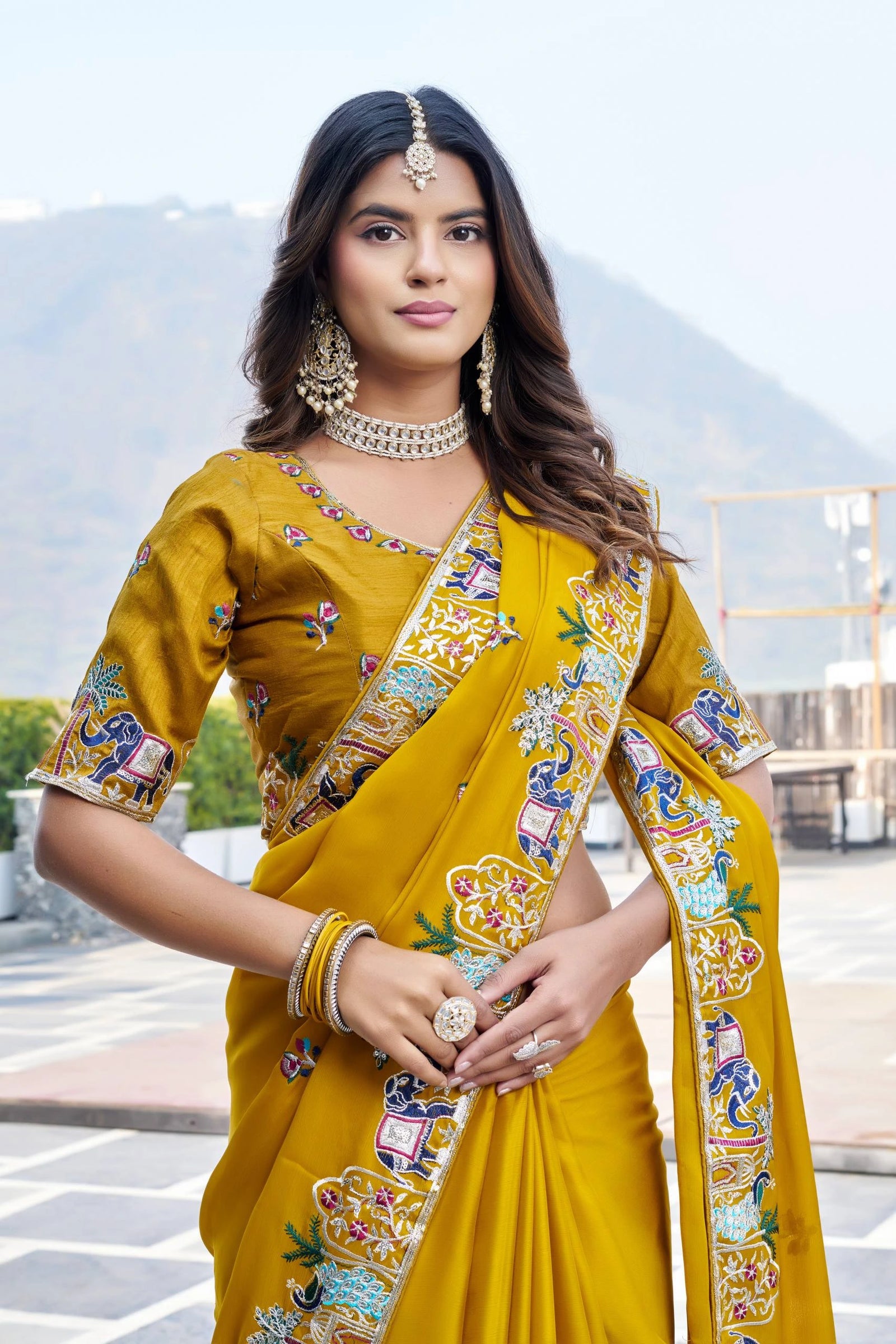 Woman wearing a yellow saree with intricate patterns outdoors.