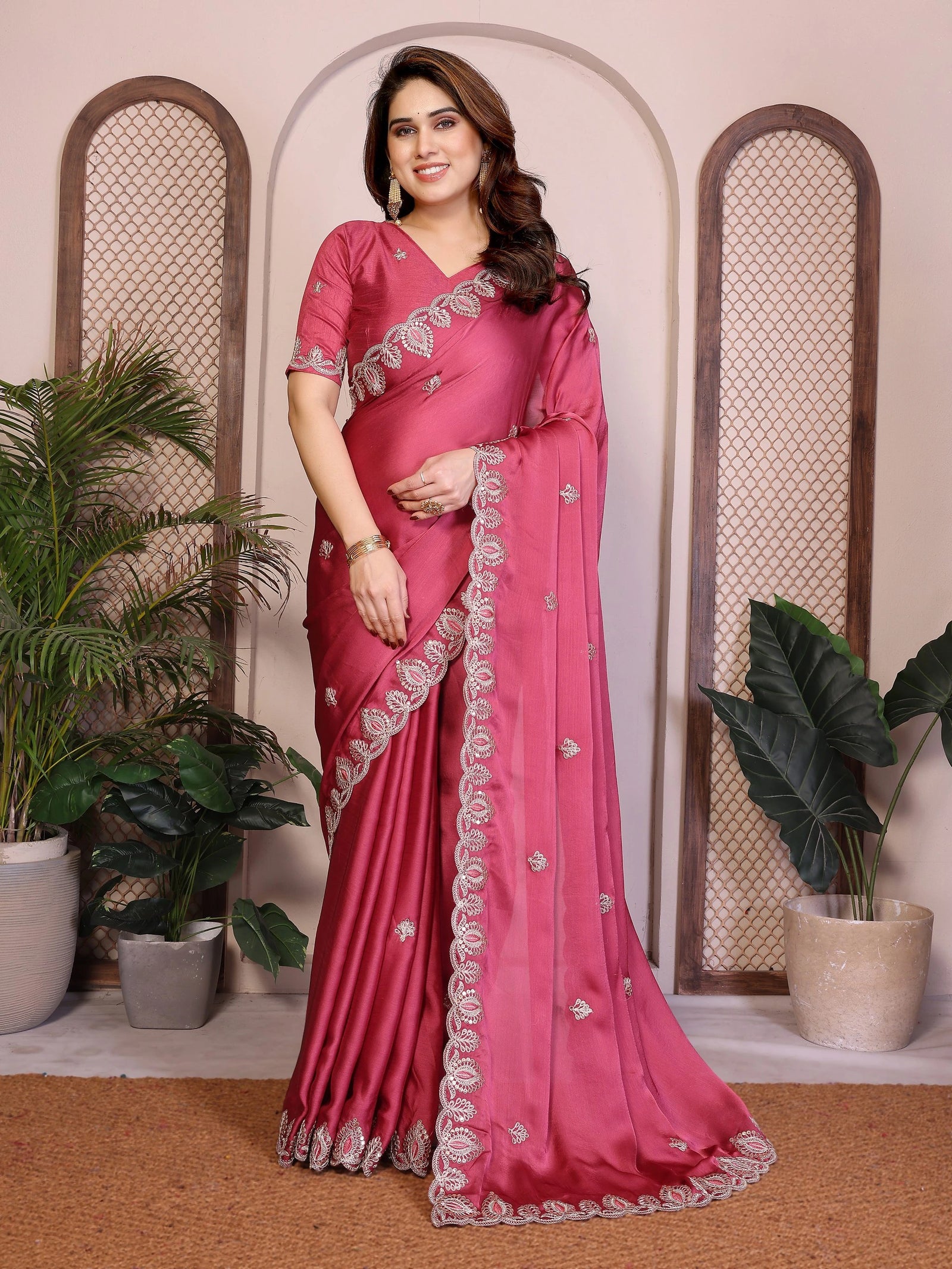 Woman wearing a pink saree with a white border indoors.