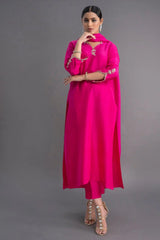 Woman wearing a bright pink traditional outfit with gold embroidery on a gray background