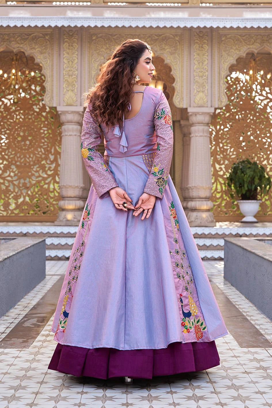 Woman in a traditional outfit with floral embroidery standing in front of an ornate architectural background.