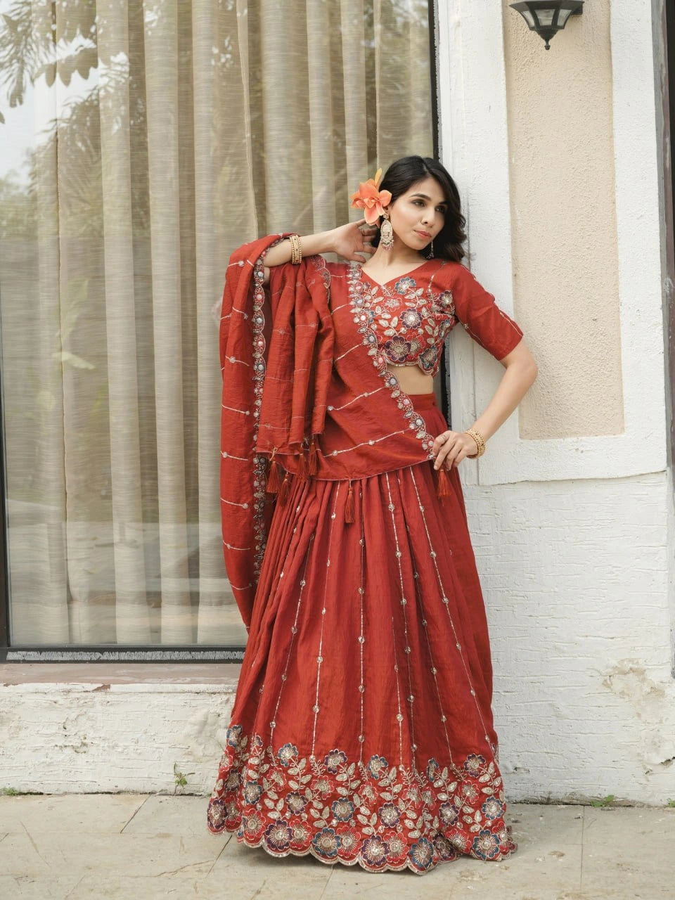 Woman in a red saree with floral patterns standing outdoors.