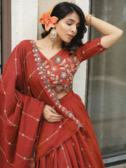 Woman in a red traditional outfit with floral embroidery, standing against a neutral wall.