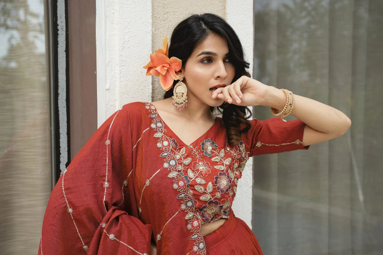 Woman in a red traditional outfit with floral accessories standing indoors.
