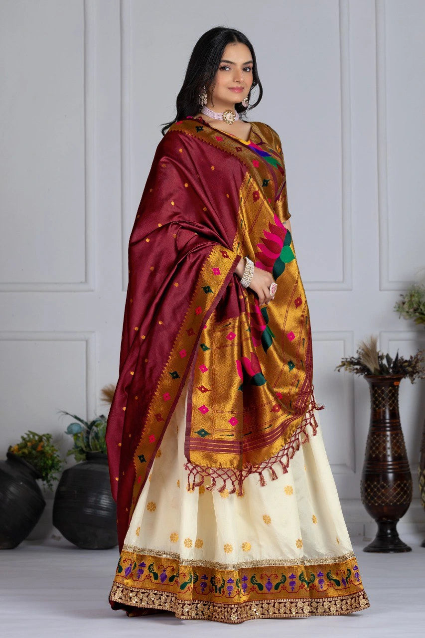 Woman wearing a traditional saree with a maroon and gold border, standing against a white paneled wall.