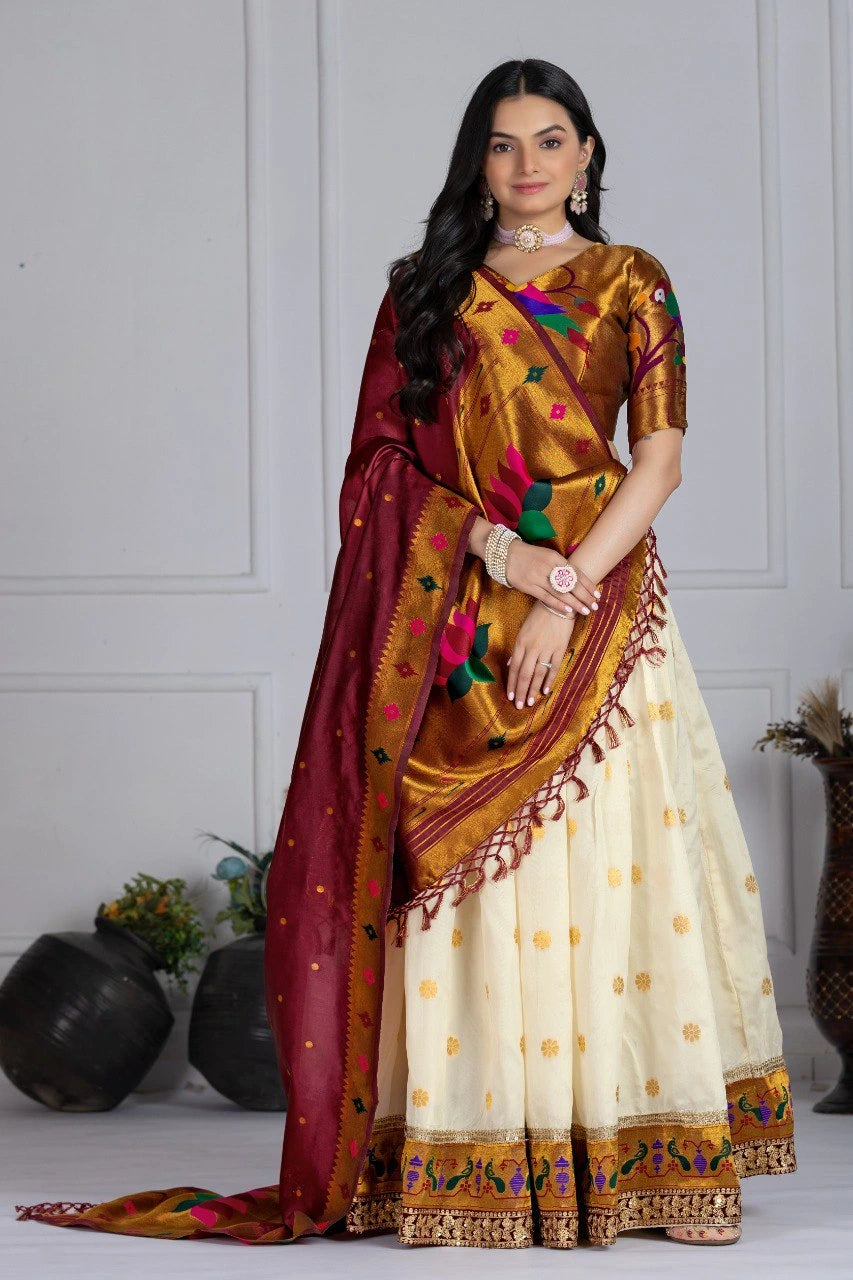 Woman wearing a traditional saree with a gold and red border, standing against a white wall.