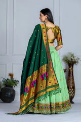 Woman wearing a green and gold saree with floral patterns against a white wall.