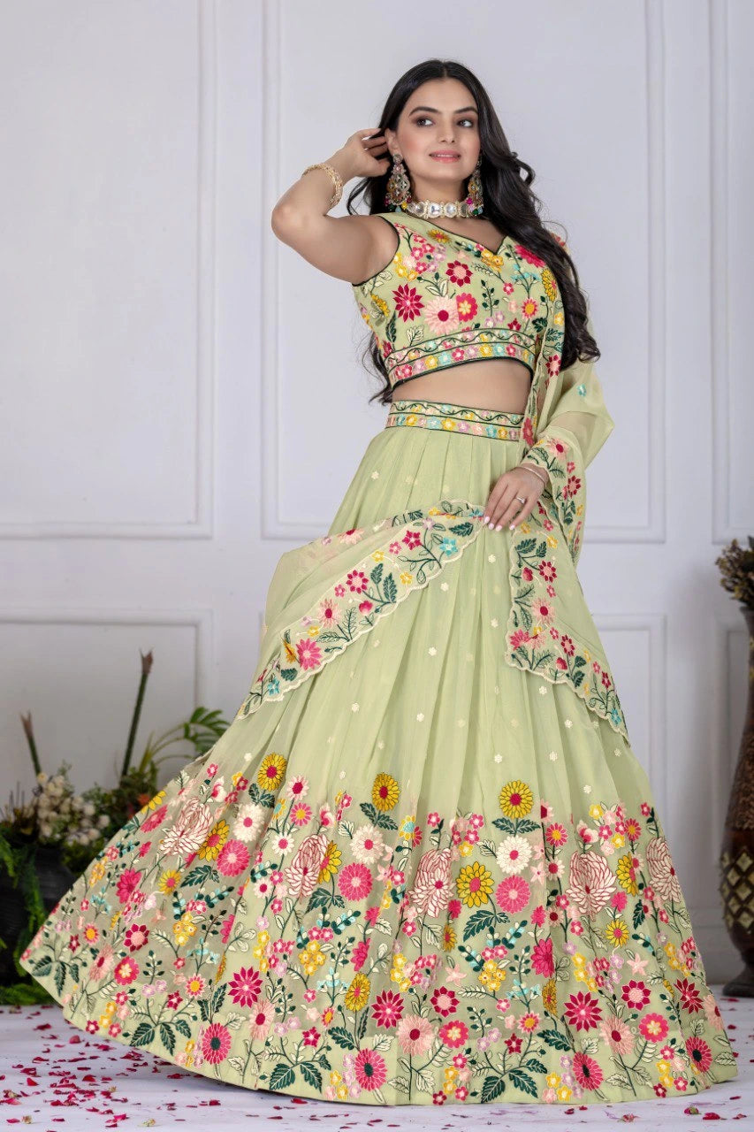 Woman wearing a floral green lehenga with a matching blouse against a white wall.