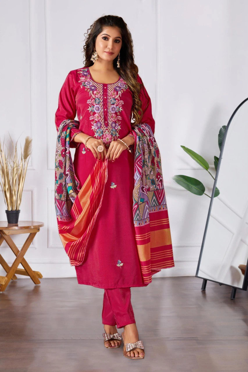 Woman wearing a vibrant pink traditional outfit with floral embroidery in a room.