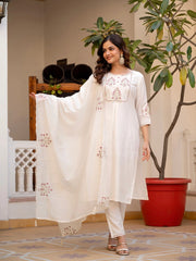 Woman in a white embroidered outfit standing indoors with plants in the background