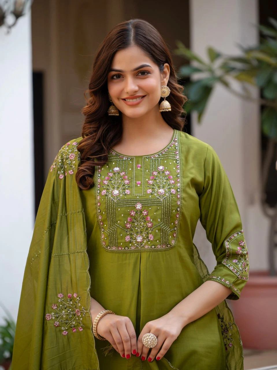 Woman wearing a green embroidered traditional outfit with a plant in the background