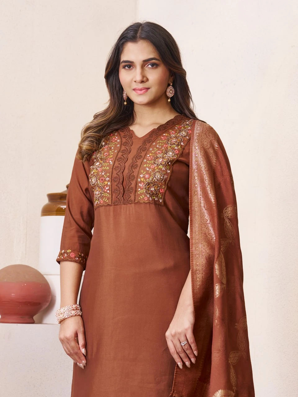 Woman wearing a brown traditional outfit with intricate embroidery on a beige background