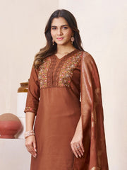 Woman wearing a brown traditional outfit with intricate embroidery on a beige background