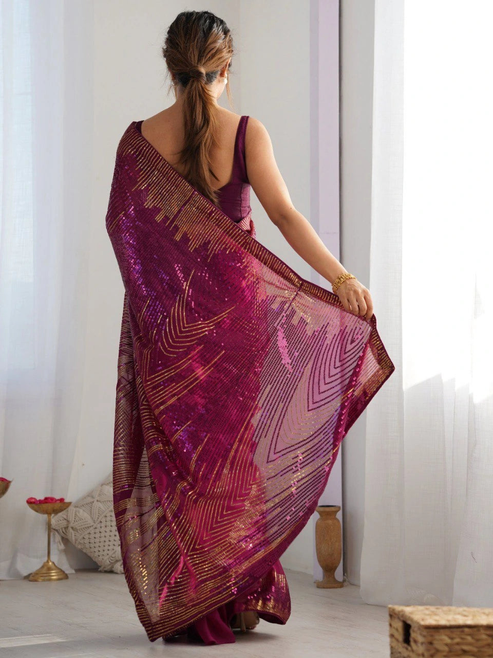 Woman holding a patterned purple scarf in a room with white curtains.