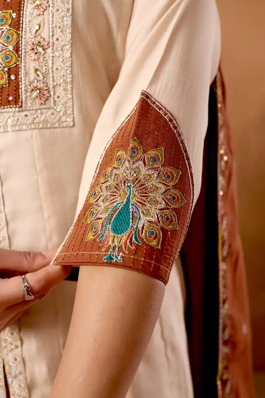 Close-up of a person wearing a traditional outfit with intricate peacock embroidery on an arm.