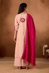 Woman wearing a peach kurta with a pink dupatta against a brown background
