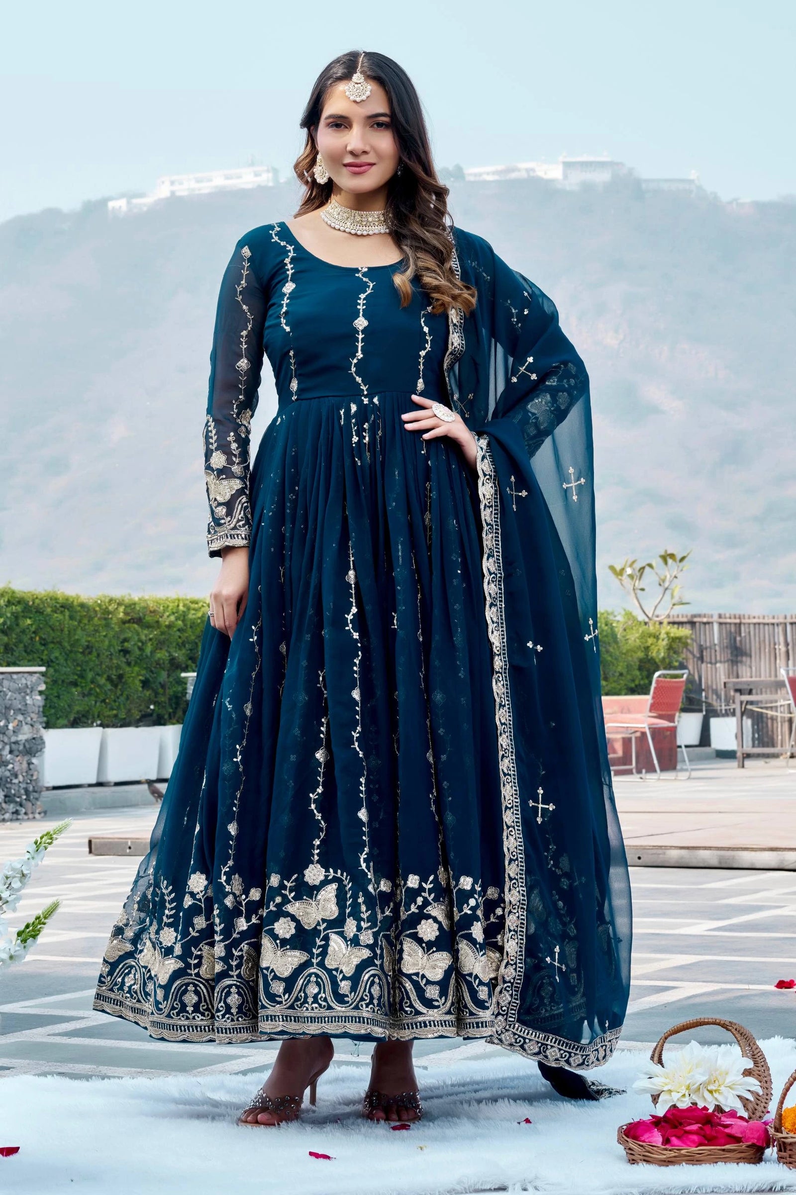 Woman in a blue traditional outfit standing outdoors with mountains in the background