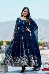 Woman in a dark blue embroidered dress standing outdoors with mountains in the background