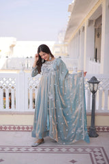 Woman in a light blue traditional outfit standing on a balcony with white railing and decorative tiles.