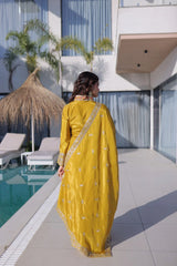 Woman in a yellow saree standing by a poolside with modern architecture in the background