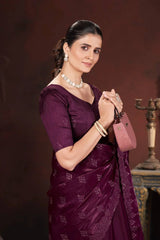 Woman in a purple saree with jewelry and a pink bag against a dark background