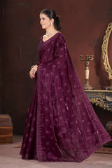 Woman in a long, dark purple embroidered dress standing against a brown background.