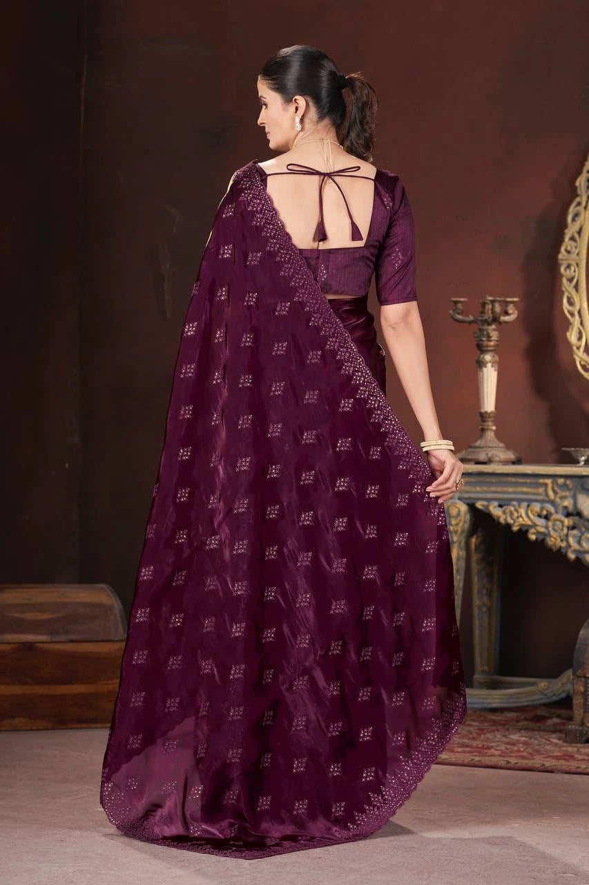 Woman wearing a purple saree with a patterned blouse, standing against a dark background.