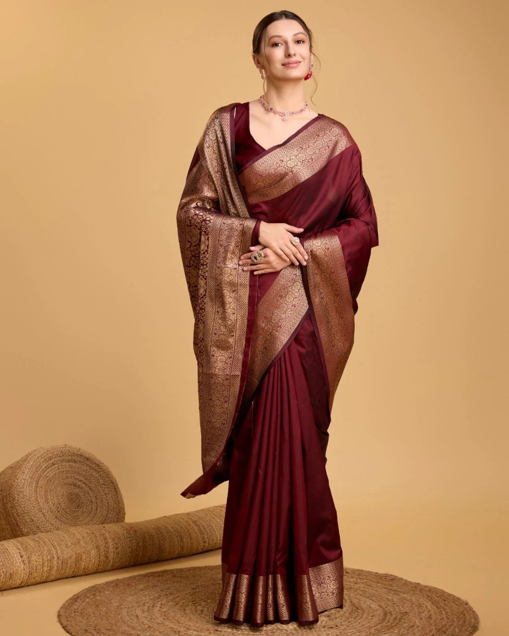 Woman wearing a maroon saree with gold border on a beige background