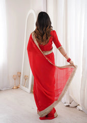 Woman in a red saree with gold border standing in a bright room.