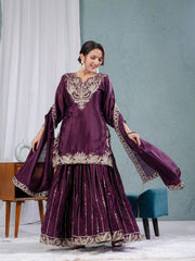 Woman wearing a purple traditional outfit with intricate designs in a minimal indoor setting.