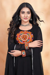Woman wearing a black outfit with colorful embroidery against a beige background