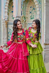 Two women in colorful traditional outfits standing in front of an ornate architectural background.