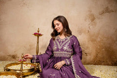 Woman in a purple embroidered dress sitting next to traditional lamps against a beige wall.