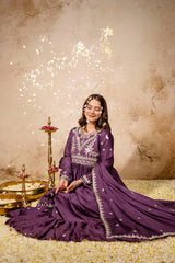 Woman in a purple traditional outfit with decorative elements, sitting on a textured floor with sparklers in the background.