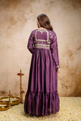 Woman wearing a purple embroidered dress against a textured beige wall.