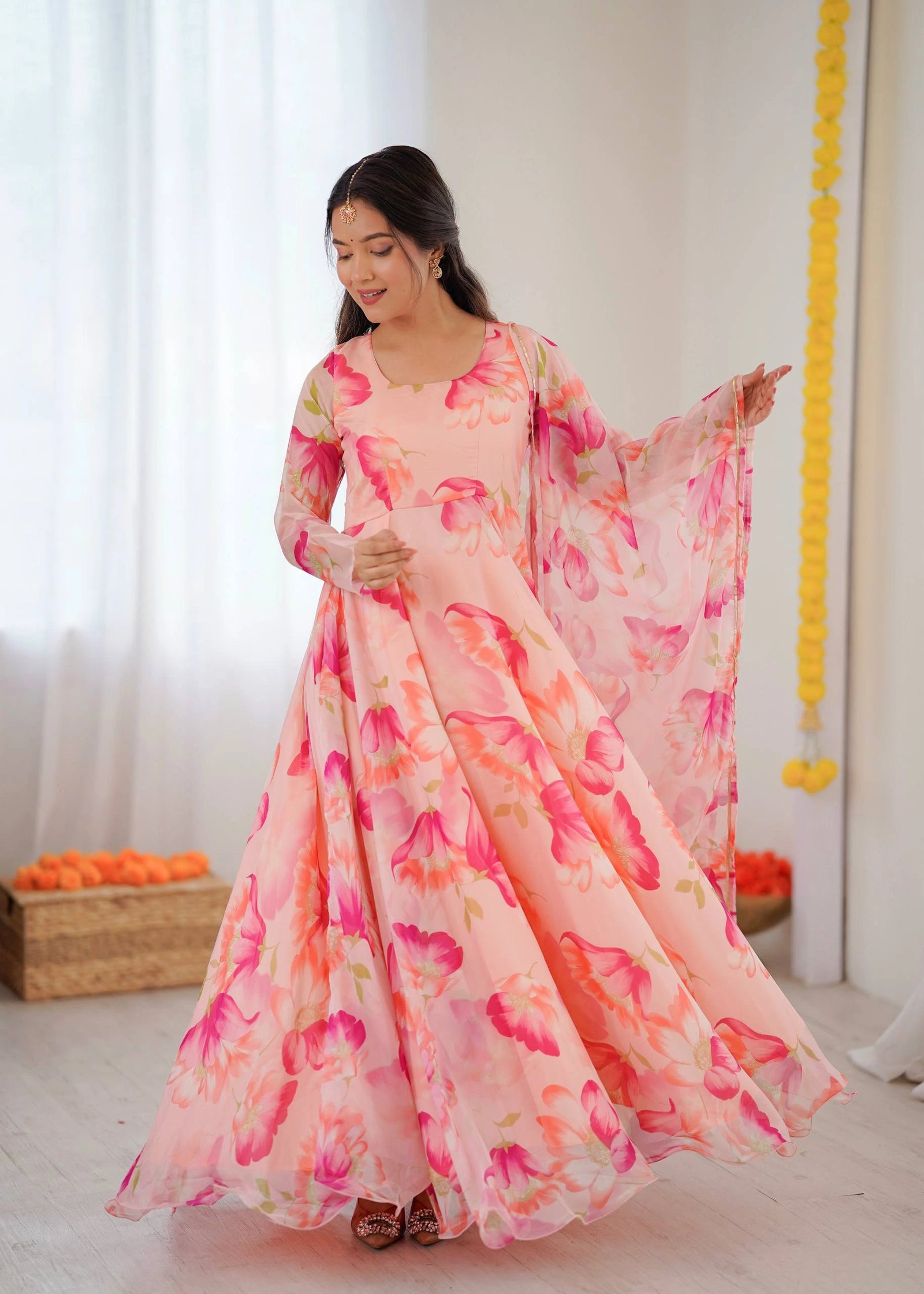 Woman wearing a floral dress in a bright room with white curtains and decorative elements.