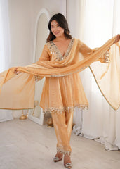 Woman in a peach-colored traditional outfit with a matching dupatta in a bright room.