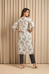 Woman wearing a white floral dress with black pants against a beige curtain background