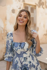 Woman wearing a blue floral dress standing outdoors with a neutral background