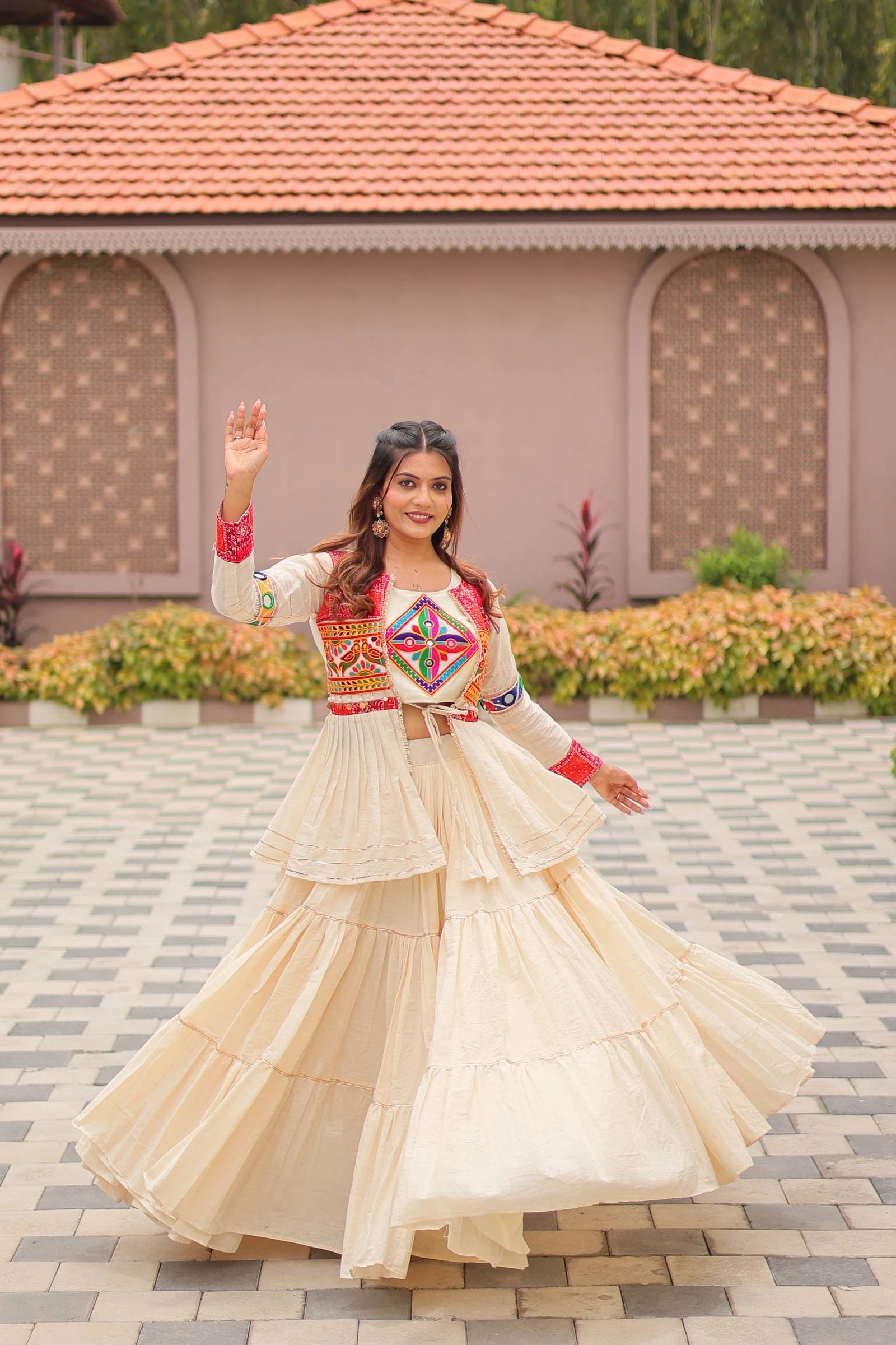 Woman in traditional outfit standing outdoors with a building and garden in the background