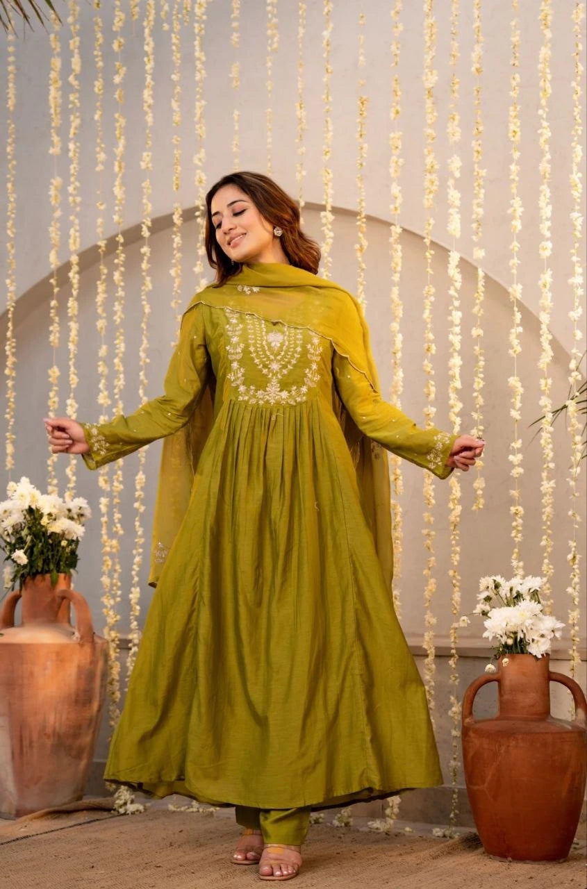 Woman in a green traditional outfit standing in front of decorative string lights and vases.