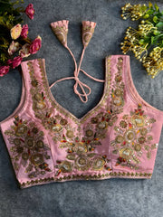 Traditional pink silk blouse featuring intricate gold zardozi embroidery and beadwork with multicolor floral and leaf motifs on the front and neckline, finished with decorative tassel ties, displayed flat on a textured grey background with artificial pink and yellow flowers in the corners.
Related
File name: vibrant-black-red-shibori-saree-tassels
Alt text: Hand-dyed black and red shibori saree with intricate tassels.