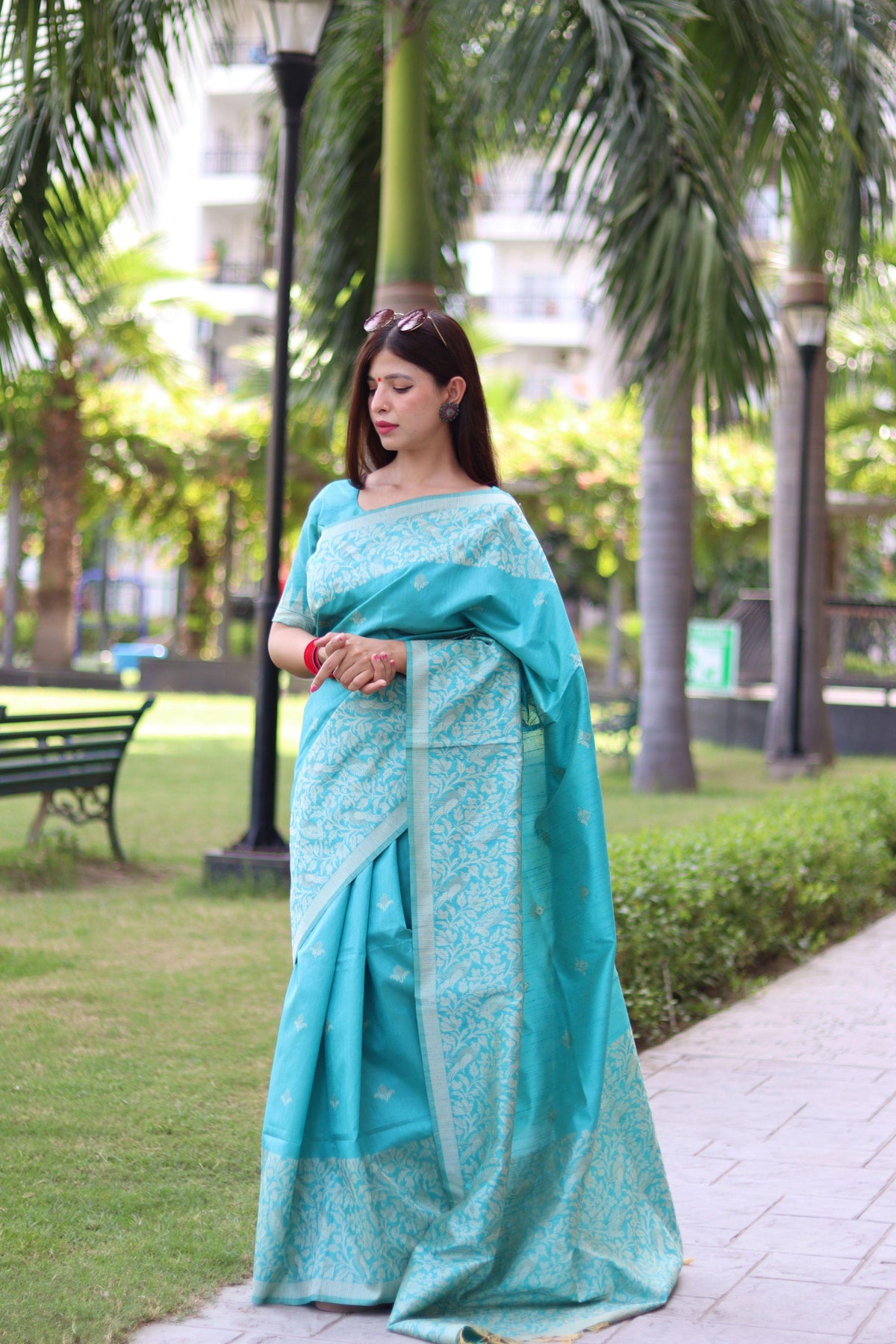 Woman in powder blue saree with traditional weaving design posing elegantly in outdoor setting