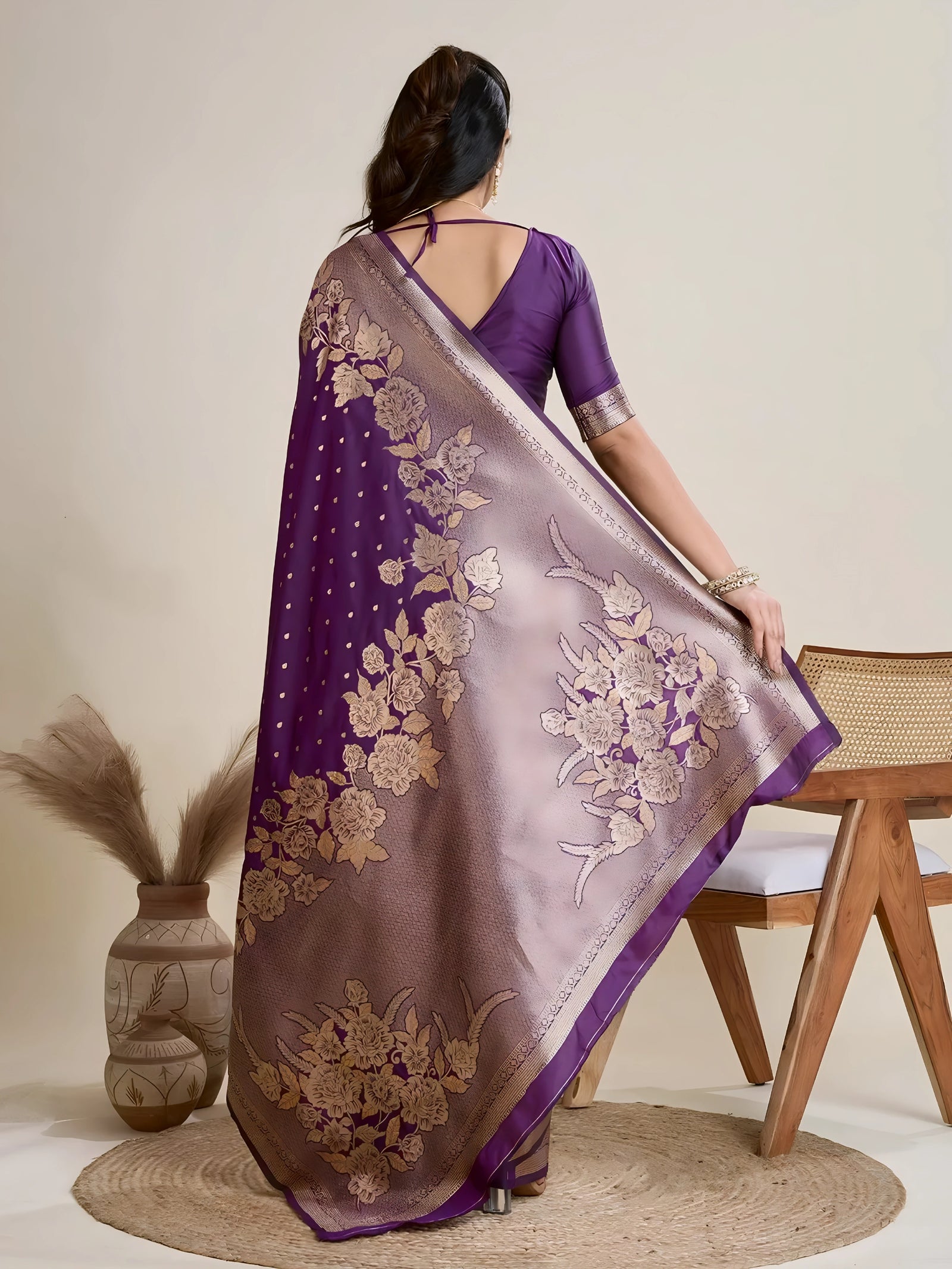 A woman models a luxurious Deep Purple Soft Kanjivaram Silk Saree. The saree features striking large floral and scattered motifs woven in metallic gold Zari on the body and wide pallu. She wears a matching purple sleeveless blouse and accessorizes with a heavy gold Kundan choker necklace and earrings.