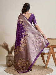 A woman models a luxurious Deep Purple Soft Kanjivaram Silk Saree. The saree features striking large floral and scattered motifs woven in metallic gold Zari on the body and wide pallu. She wears a matching purple sleeveless blouse and accessorizes with a heavy gold Kundan choker necklace and earrings.