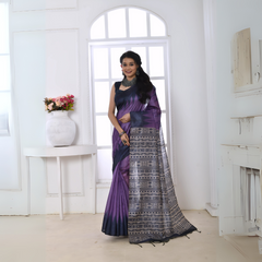 A woman models a striking Purple Soft Tussar Silk Saree. The saree features a color-block transition between purple and deep navy/black. The pallu has a wide panel of dense, grey and black geometric Ikat-style print. She wears a dark sleeveless blouse and chunky oxidized silver jewelry.