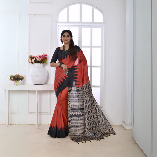 A woman models a striking Terracotta Red Soft Tussar Silk Saree. The saree features a bold black zigzag pattern along the border and a pallu with dense geometric black and white tribal-style print. She wears a black blouse and chunky oxidized silver jewelry, posing indoors by a large window.