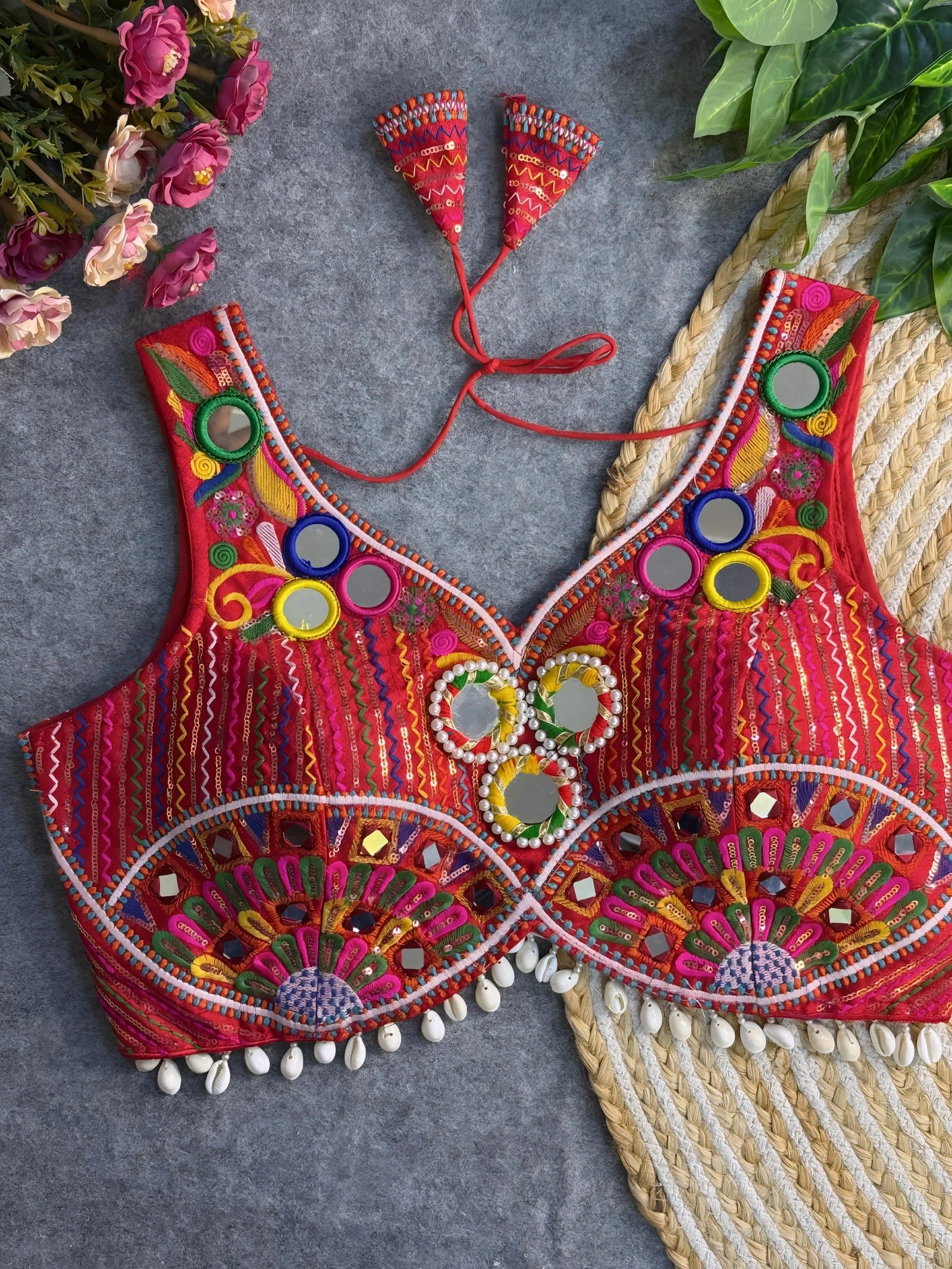 Traditional red blouse featuring vibrant multicolor mirror work, intricate thread embroidery in geometric and floral patterns, and shell tassel detailing along the hem, displayed on a flat surface with floral and leafy decor.
Related
red-multicolor-mirror-work-embroidery-blouse-shell-tassels
Traditional red blouse with vibrant mirror work, detailed embroidery, and shell tassel accents.