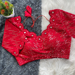 Red bridal blouse with scallop sleeves, featuring silver sequin stripes and prominent round mirror work along the neckline, sleeves, and hem, displayed on a textured grey and white fur background with a small potted plant nearby.