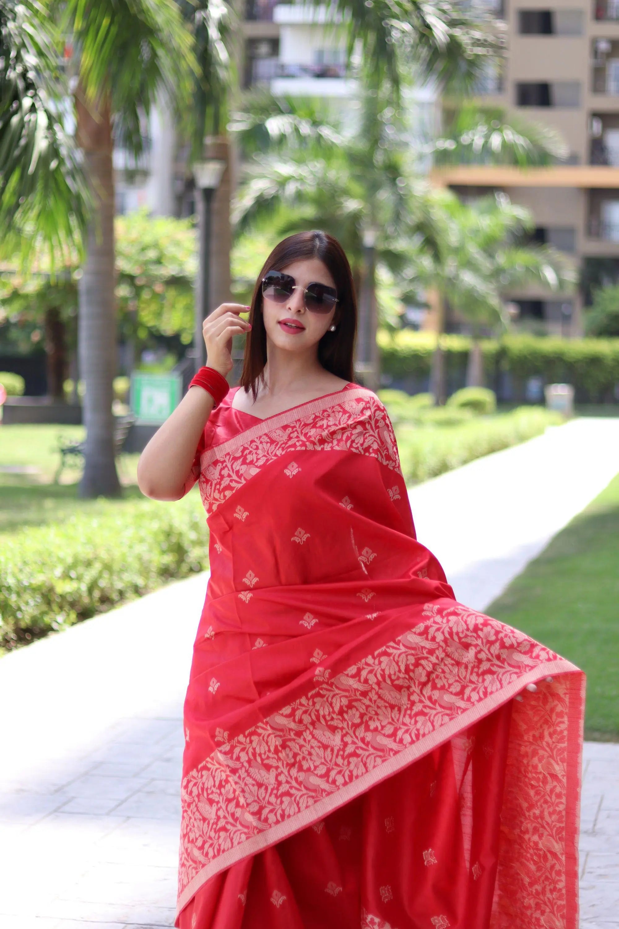 A red silk saree featuring traditional weaving patterns, elegantly draped and showcased in an outdoor setting.